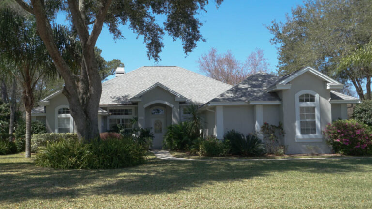Exterior view of a finished home with a new roof surrounded by grass and one large tree in front of the house.