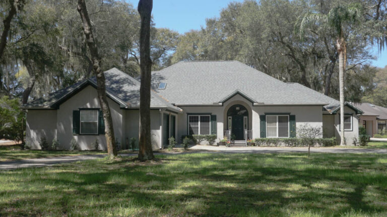 Exterior view of a finished home with a new roof and skylight surrounded by grass and various tall trees.