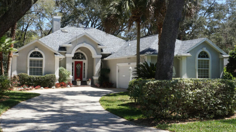 Exterior view of a finished home with a new roof surrounded by grass and numerous large trees with a wide walkway to the front door.