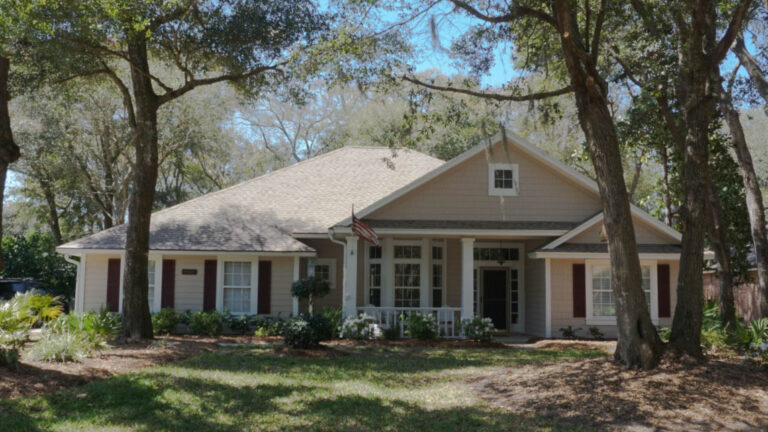 Exterior view of a finished home with a new roof surrounded by grass and numerous large trees.