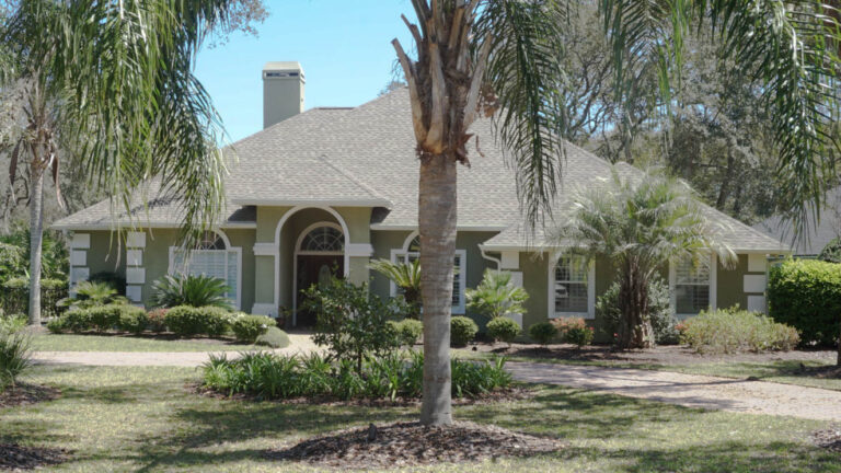 Exterior view of a finished home with a new roof surrounded by grass and numerous trees around the home.
