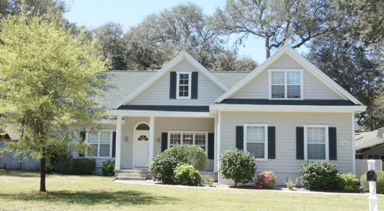 Exterior view of a finished home with a new roof and siding surrounded by grass and trees.