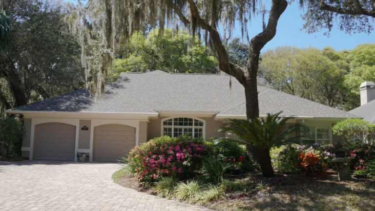 Exterior view of a finished home with a new roof surrounded by numerous trees around the home along with a large drive-way and garage to the home.
