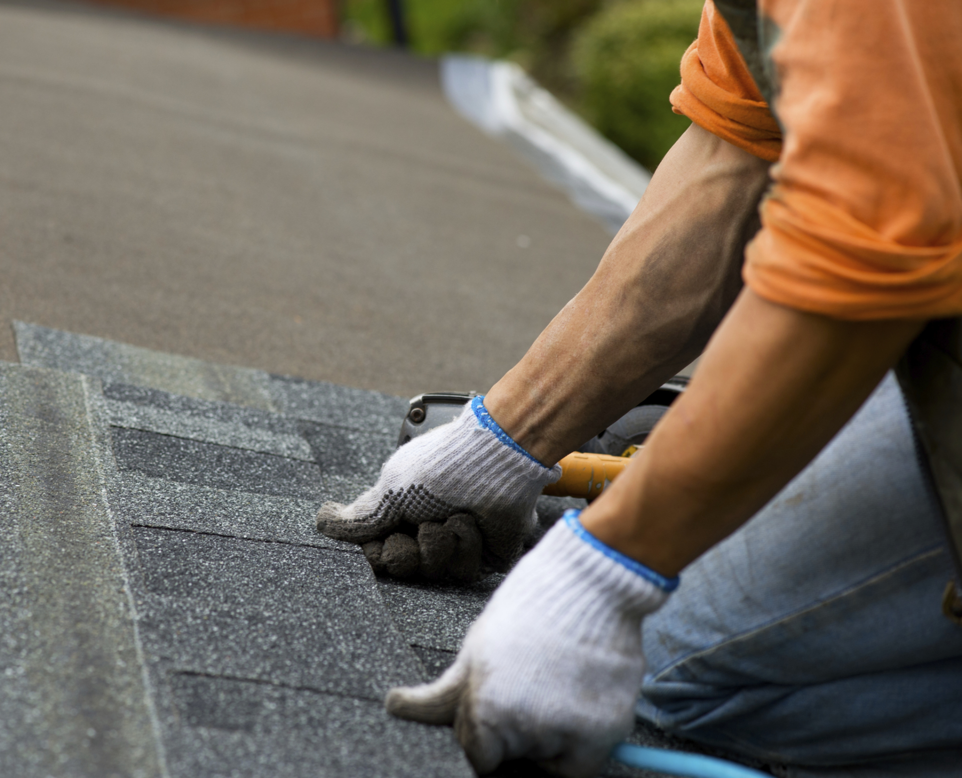 A person installing roof shingles on a roof with his hands and proper safety equipment